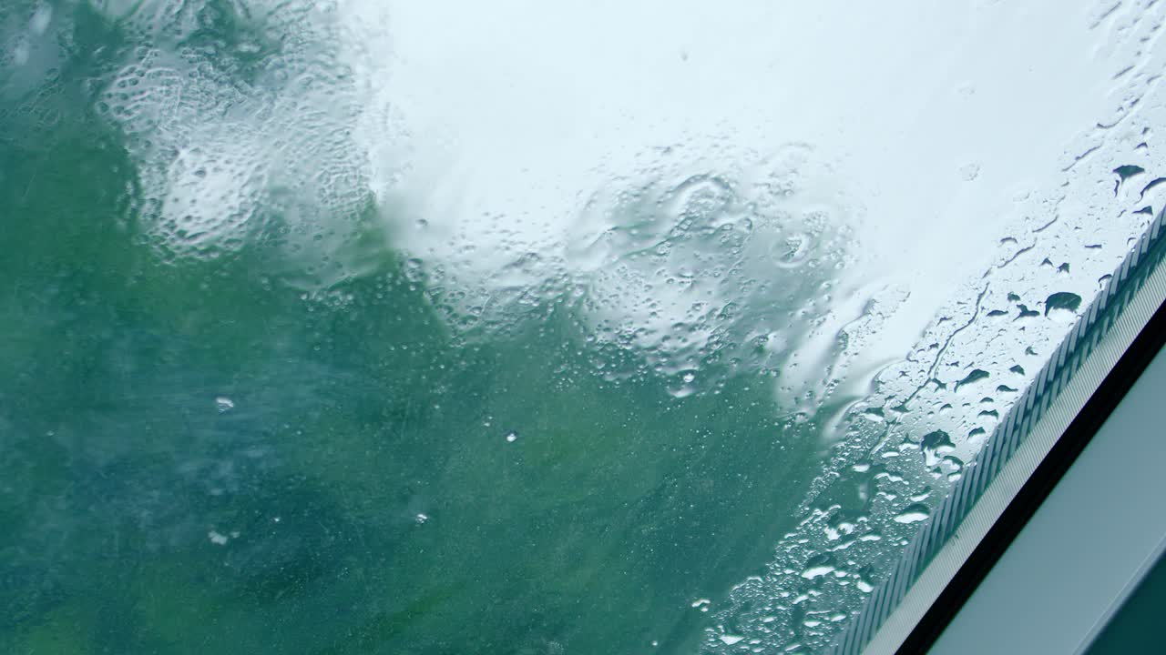 Raindrops hitting glass surface and running down. Close up, handheld