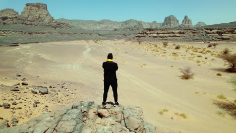 Man-Standing-On-The-Edge-Of-A-Cliff-In-Djanet-Desert-In-Algeria---aerial-pullback