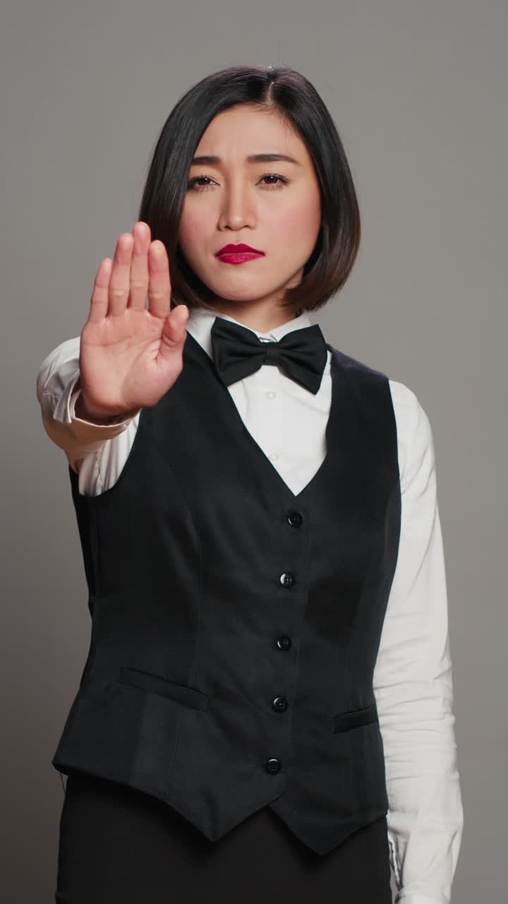 Vertical Video Asian administrator showing stop sign with palm raised in studio,