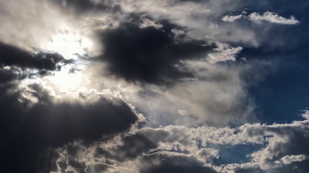4K UHD timelapse capturing dynamic weather as brilliant sun rays ripple through rapidly shifting dark clouds. The dramatic sky illustrates intense atmospheric and climate activity.