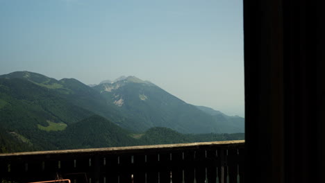 cinematic view looking out of a window at koča na golici hut in the karavanke mountains, slovenia. the shot reveals peaceful alpine scenery, mountain slopes, and lush green landscape.