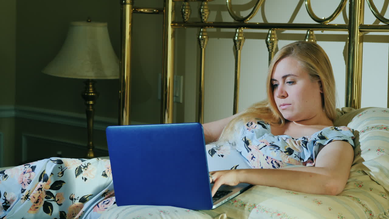 Young Woman With Laptop Resting In Bed In Her Bedroom