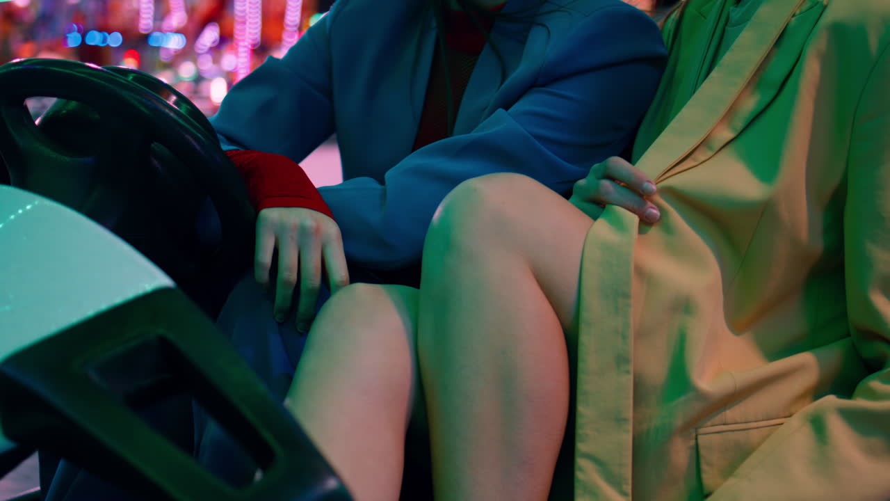 Closeup female legs body in bumper car carousel. Two girls rest luna park night