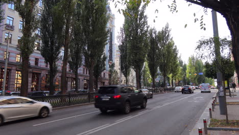 busy street with tall trees and many cars driving in kyiv city center ukraine, khreshchatyk area, 4k static shot