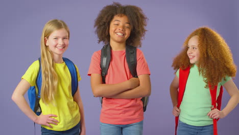 foto de estudio de tres niños con mochilas yendo a la escuela con fondo púrpura