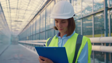 Woman-engineer-making-notes-analysing-production-data-in-modern-glasshouse