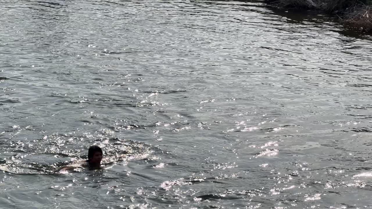 A man swims through sparkling river water under bright sunlight in a wide outdoor shot