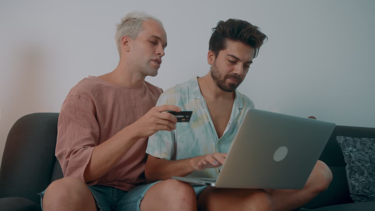 Two men shopping online together on a sofa.