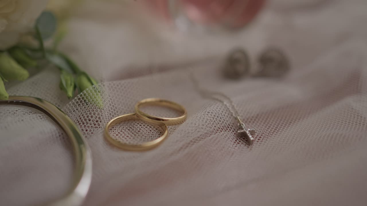 부드러운 얇은 명주 위에 놓인 금색 결혼 반지, 목걸이, 귀걸이는 사랑, 결합, 우아함을 상징해요.