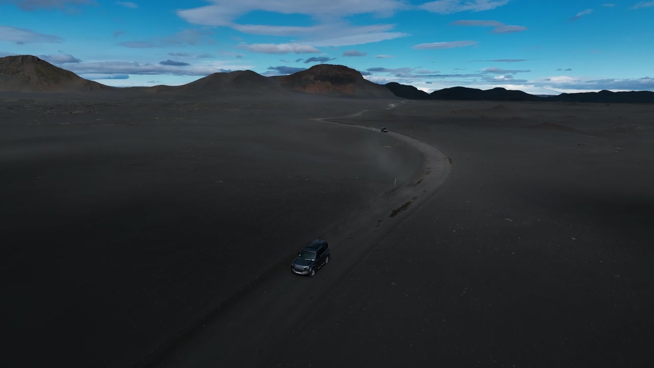 Off-road SUV car driving in volcanic sand desert and black hills in Iceland. Exploring nordic geology.