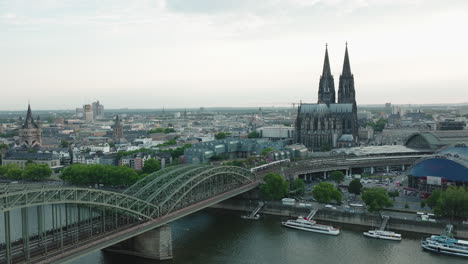 drone moves to the right, the cologne cathedral in gloomy weather is in the center, the hohenzoller bridge with the rhine is in the lower part of the picture