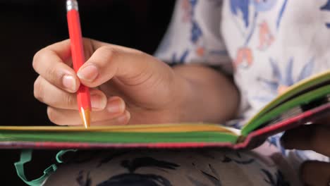 primer plano de la mano de una persona escribiendo en un cuaderno con un lápiz rojo