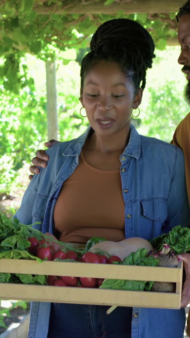 Vertical video: Leaning man urging woman in denim checking radishes in crate under pergola selling
