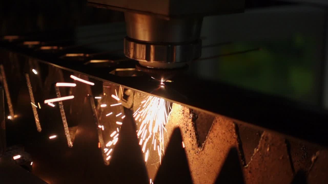 Burning sparks flying from plasma laser cutting precise lines in metal sheet