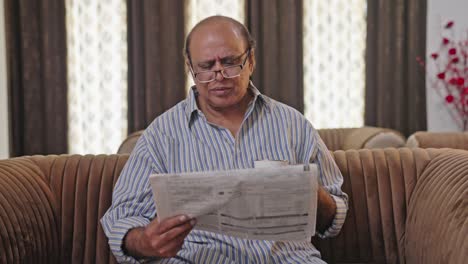 Upset-Indian-old-man-reading-newspaper-in-morning