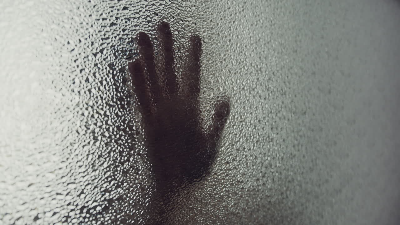 A female silhouette behind the frosted window touches the glass slowly