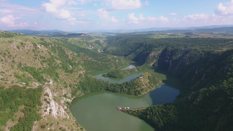 high altitude view of uvac river in europe serbia with small buildings by the green water, aerial forward slow