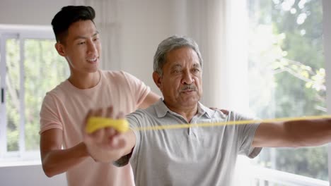 diverse male physiotherapist advising and senior male patient using exercise band, in slow motion