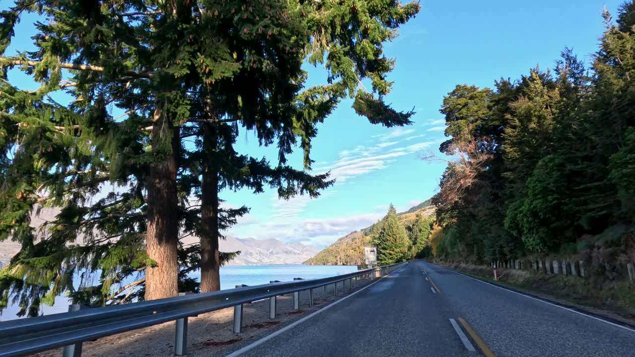 Car drives scenic lakeside mountain road, clear daylight, wide angle, smooth forward camera movement