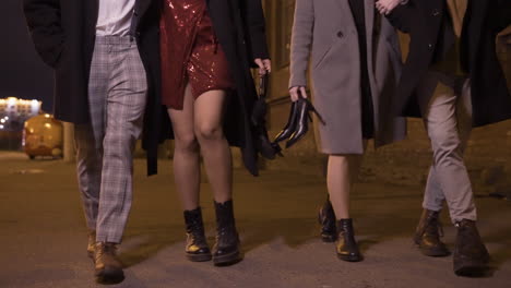 camera focuses on the feet of four friends walking in the street after the end of the year party