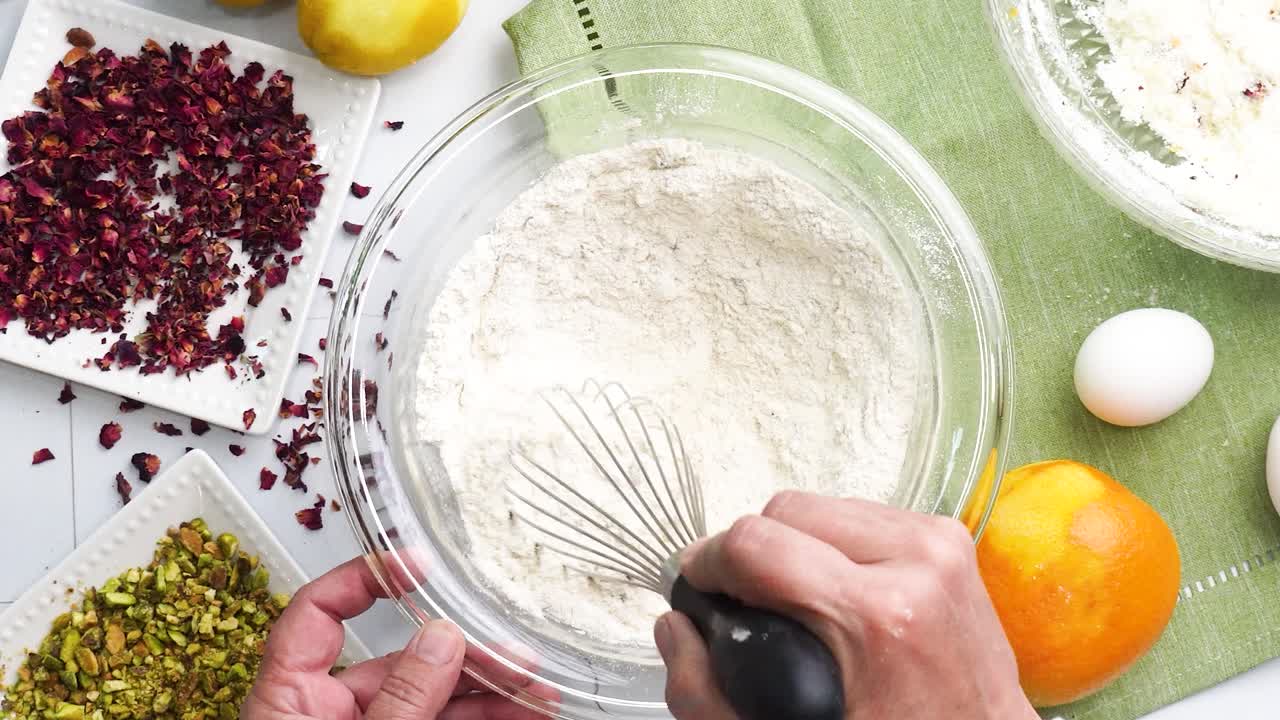 Baking a dessert called Persian Love Cake made with rose petals and pistachios. Cake with white glaze frosting. Mixing in the ingredients with a whisk. Beautiful cake for tea time or celebration