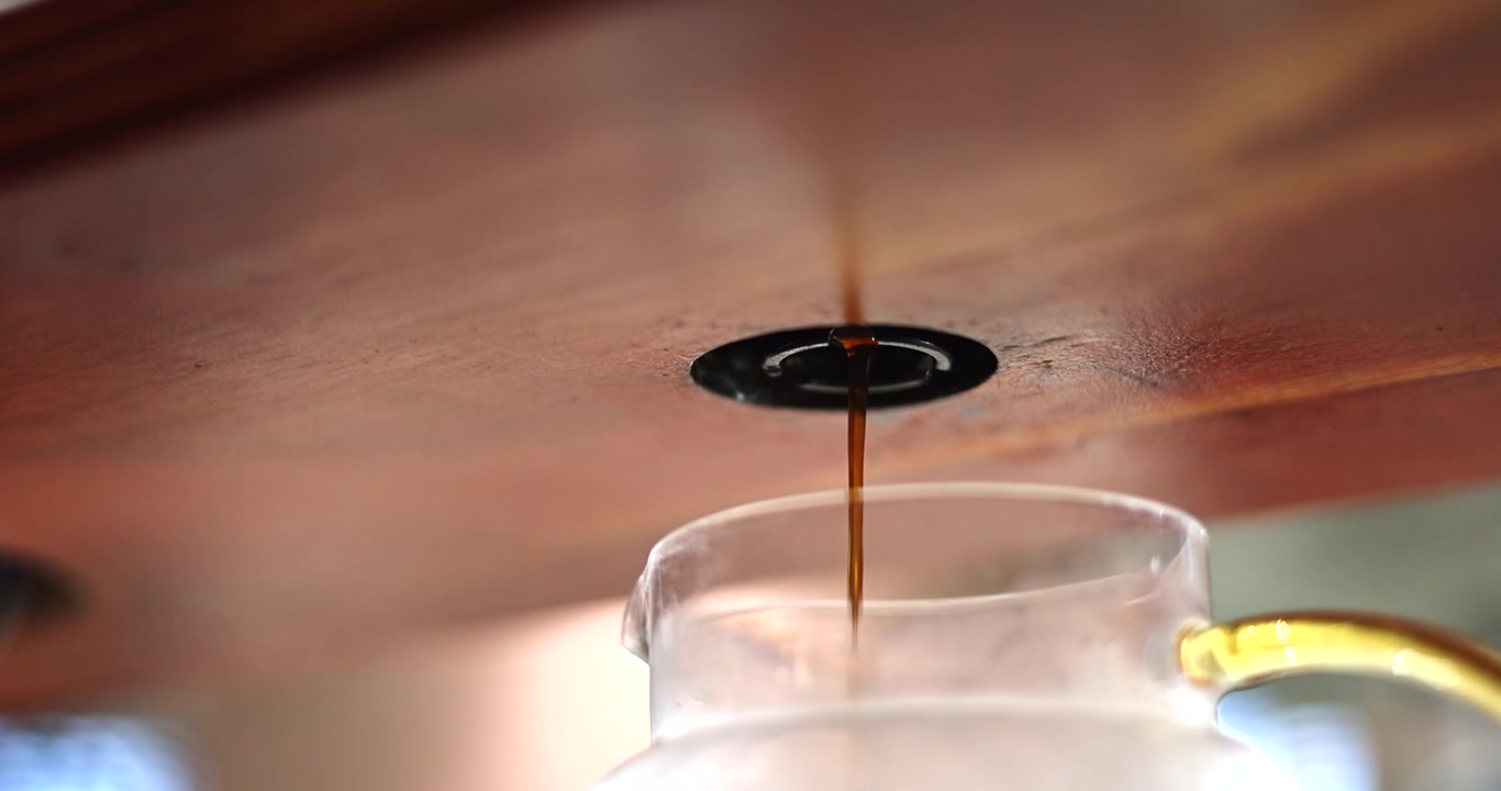 Il caffè appena fatto scorre dolcemente dalla macchina da caffè in una caraffa di vetro sotto un bancone di legno.