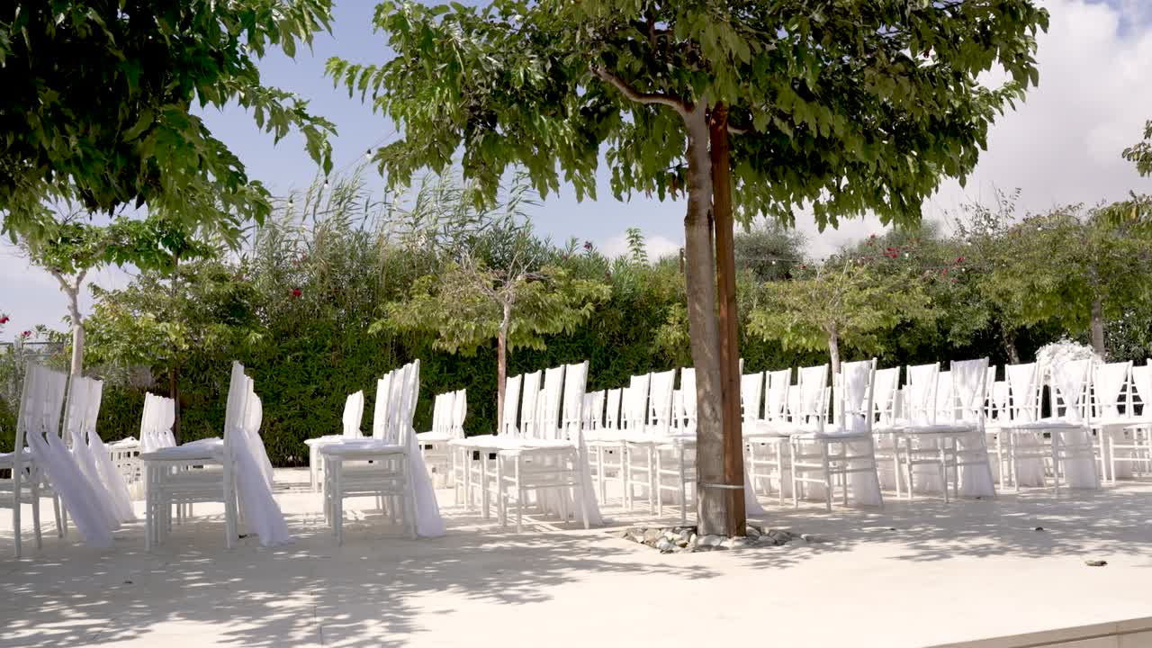 Uno spazio esterno è allestito per un matrimonio, con numerose sedie bianche disposte sotto gli alberi. Una splendida vegetazione circonda l'area, creando un'atmosfera di calma per gli ospiti.