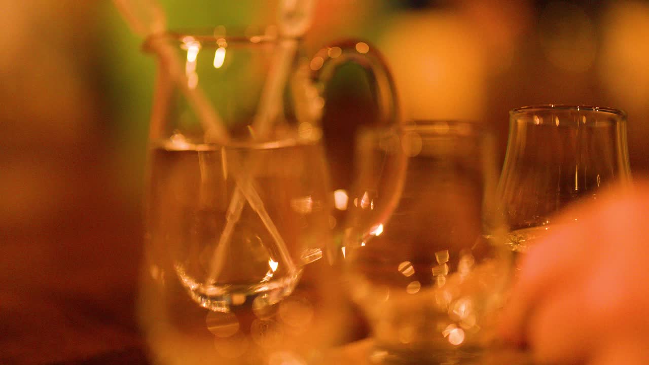 A hand reaches for a whisky glass beside a water jug under warm ambient lighting