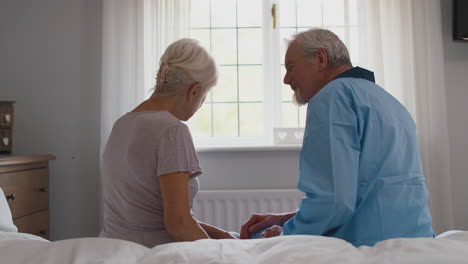 worried retired senior couple sitting on bed at home talking together