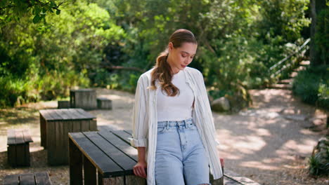 calm woman standing sunny park leaning on wooden table. girl dreaming on nature