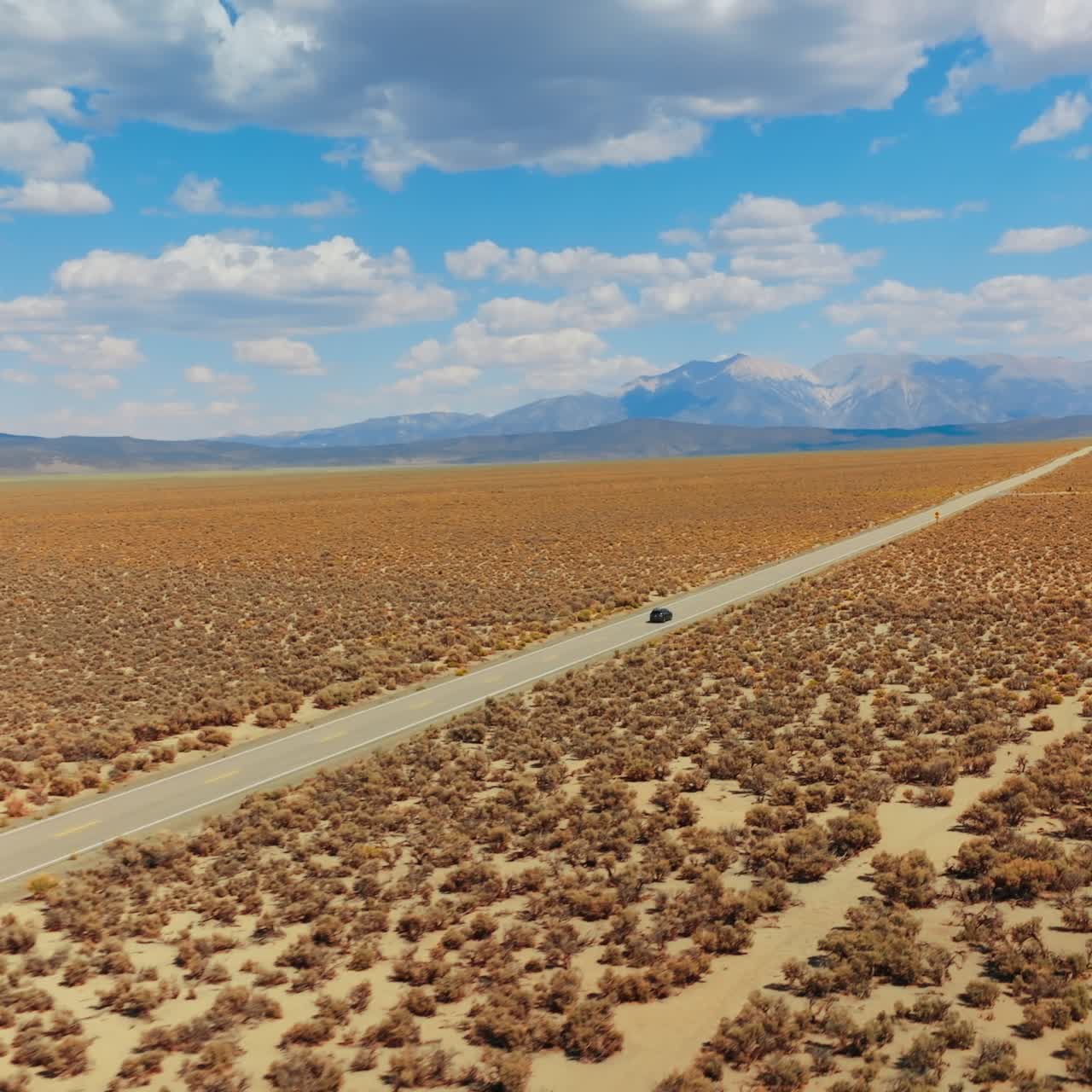 Long straight road in the lifeless desert. Highway to Nevada from California. Beautiful landscape at backdrop of blue skies with white clouds