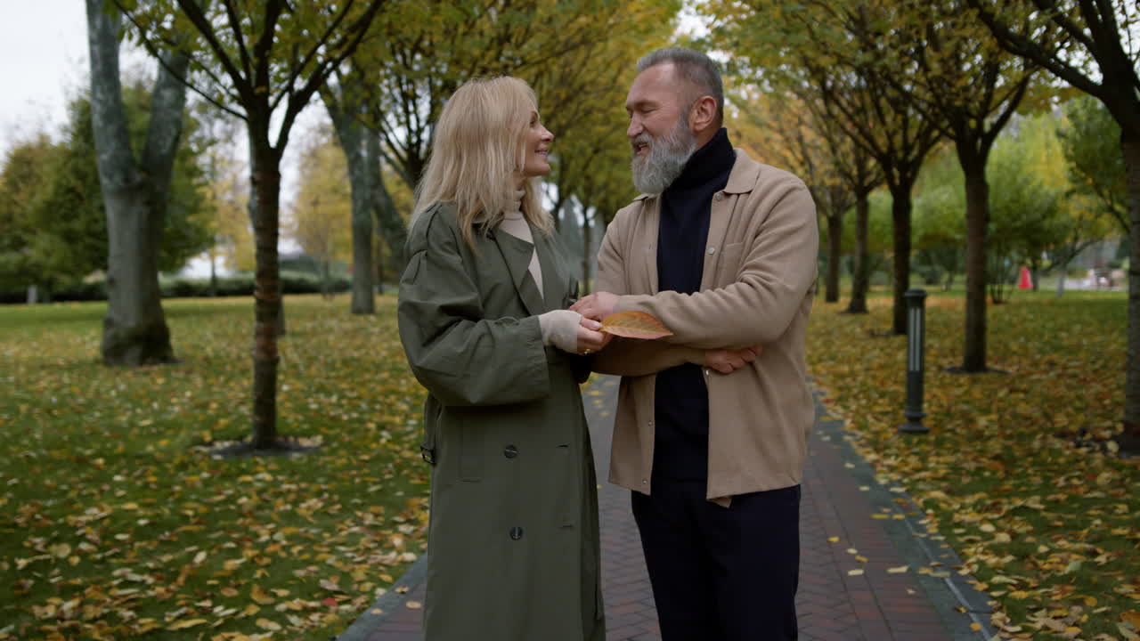una pareja sonriente de amantes divirtiéndose con gestos activos de la mano en el parque de otoño.