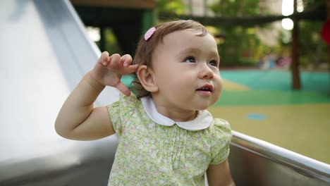 Happy-excited-little-girl-sitting-on-a-slide-daytime-and-showing-her-happy-face-to-camera-on-sunset-in-Playground