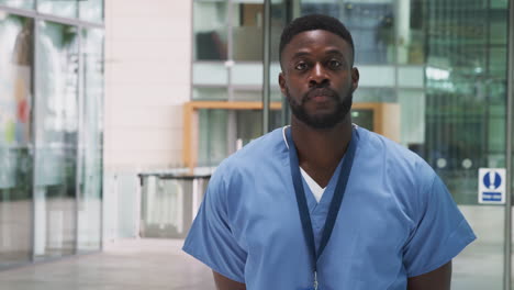 Portrait-Of-Male-Nurse-Wearing-Scrubs-Standing-In-Modern-Hospital-Building