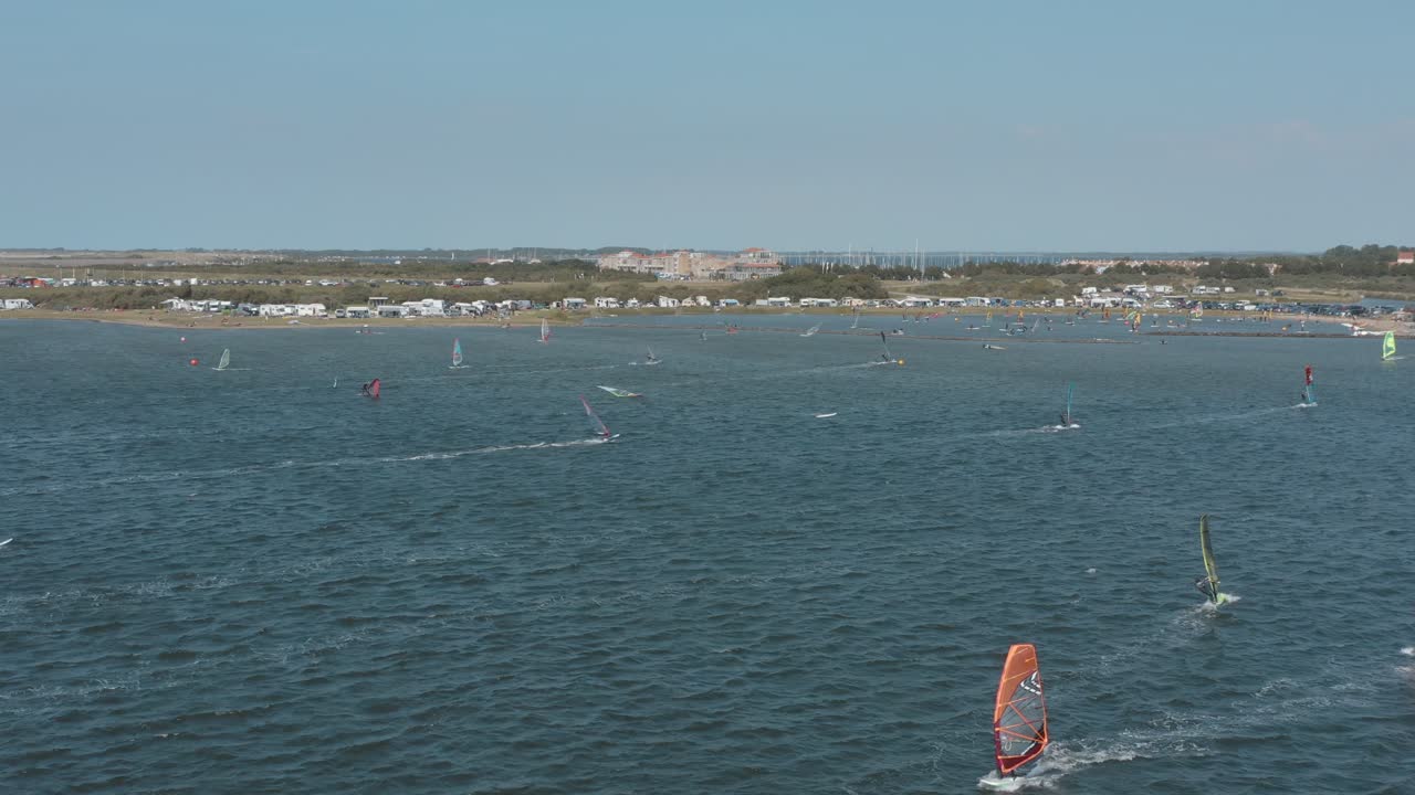 drone - toma aérea de muchos surfistas en un mar azul, ondulado y ventoso en un día soleado con nubes blancas en una isla, zelanda, países bajos, 25p