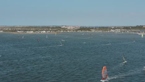 Drone---Aerial-shot-of-many-surfers-on-a-blue,-wavy-and-windy-sea-on-a-sunny-day-with-white-clouds-on-a-island,-Zeeland,-Netherlands,-25p