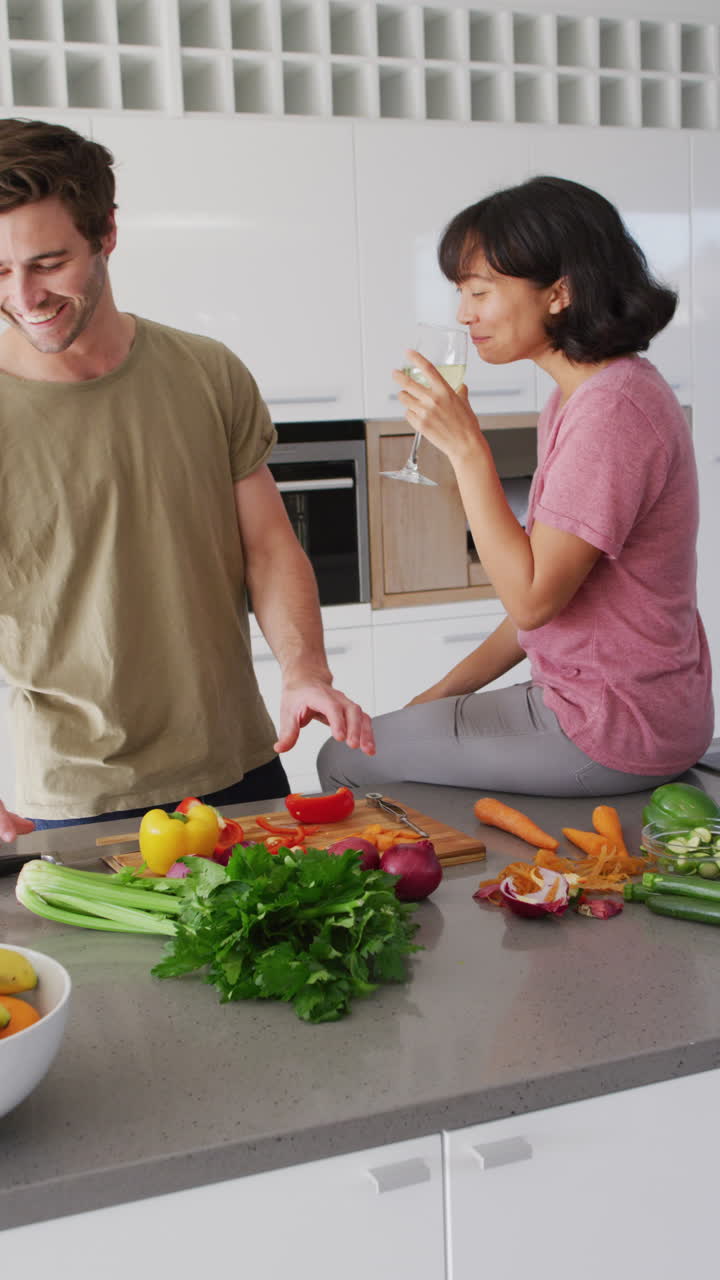 video vertical de una pareja feliz y diversa cocinando juntos y bebiendo vino