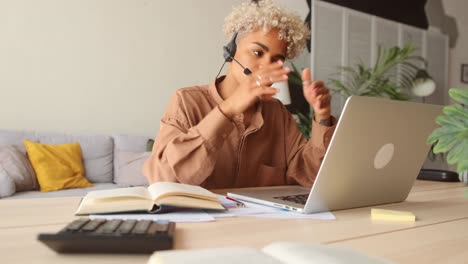 afro businesswoman wear headset talk by conference call via laptop at home