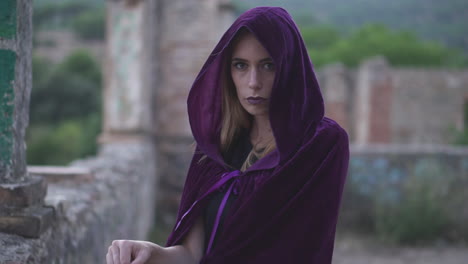 mysterious young woman wearing a cloak and a hood covering her head staring at the camera and holding an old lantern