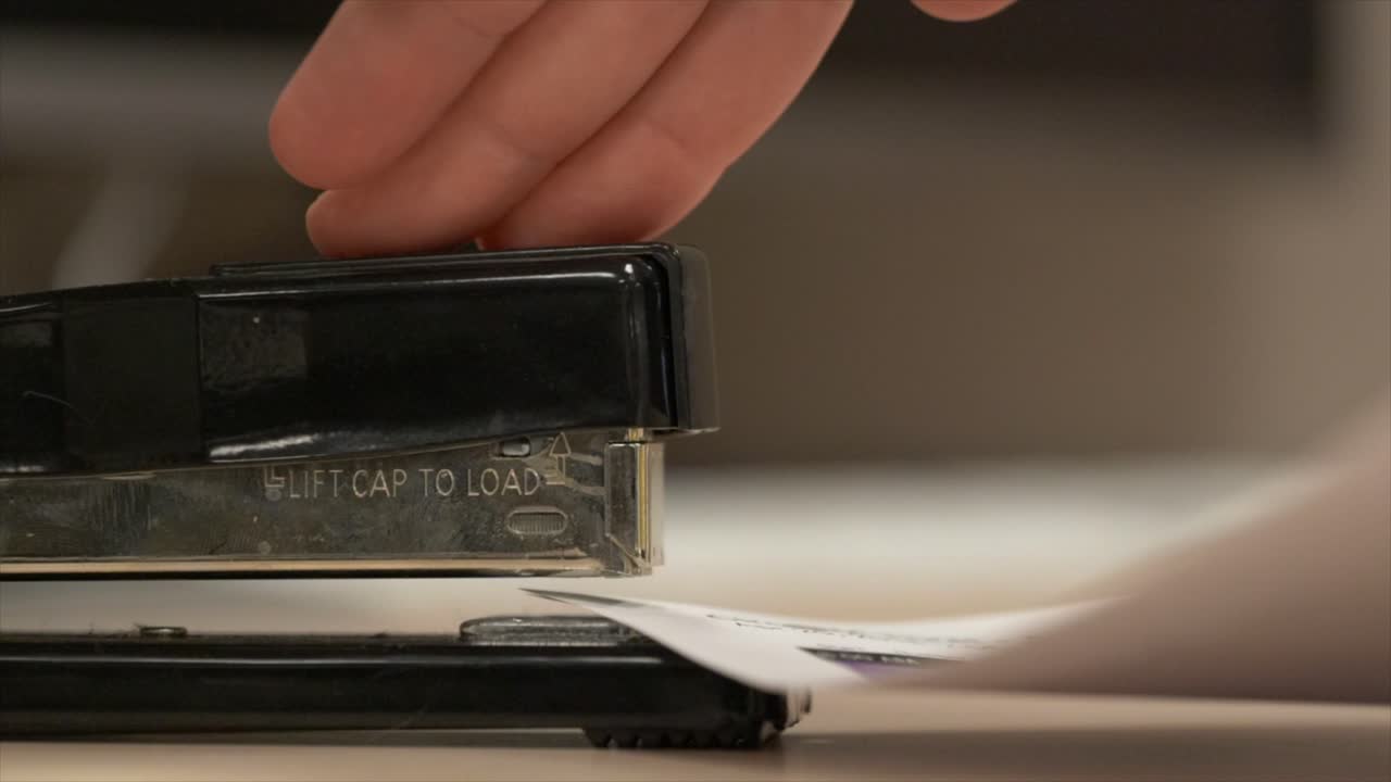Side view of a black stapler stapling some paper together in really slow motion