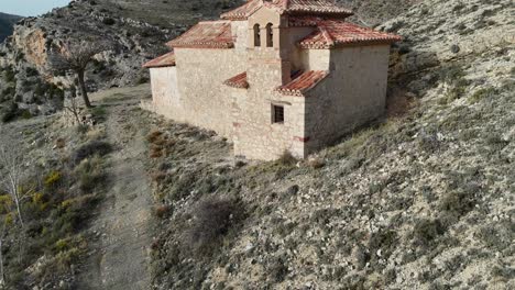disparo aéreo de avión no tripulado volando hacia atrás de una ermita aislada en un paisaje árido