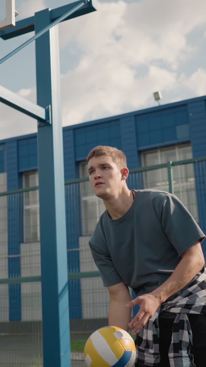 jugador de voleibol durante una sesión de entrenamiento rebotando la pelota de voleibor, girándola en la mano antes de lanzarla y golpearla, capturado al aire libre en una arena deportiva con una cancha de baloncesto en el fondo