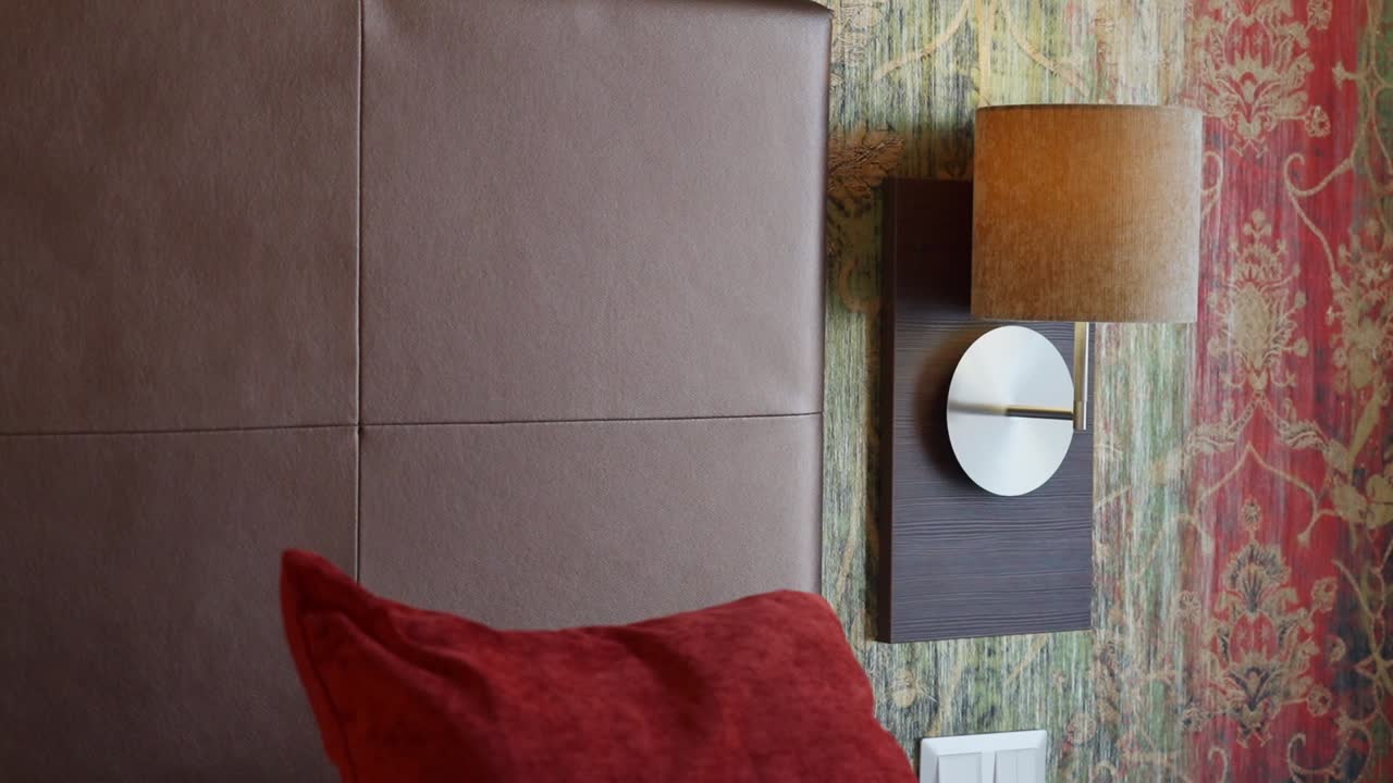 Close-up of a bedside lamp with red pillow and colorful wallpaper