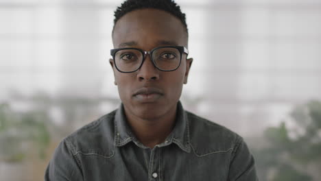 portrait of young african american business student intern man turns head looking serious pensive at camera wearing glasses in office workplace background