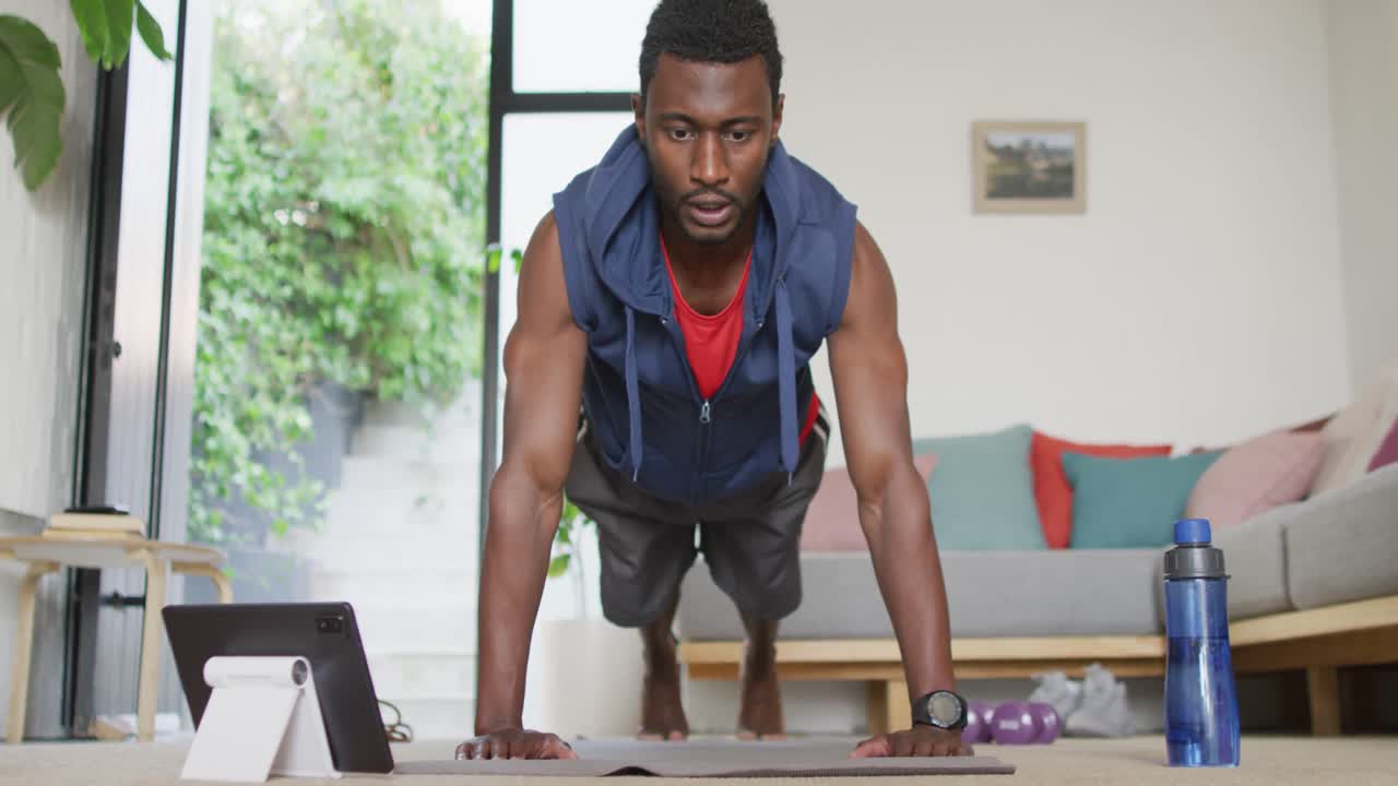 Happy african american man exercising in living room, using tablet