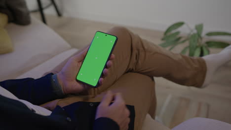 man sitting on sofa gets cellphone with green screen