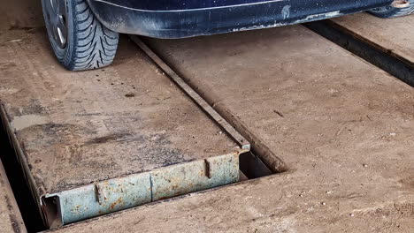 dirty scissor lift platform rises with vehicle parked above an open car repair pit