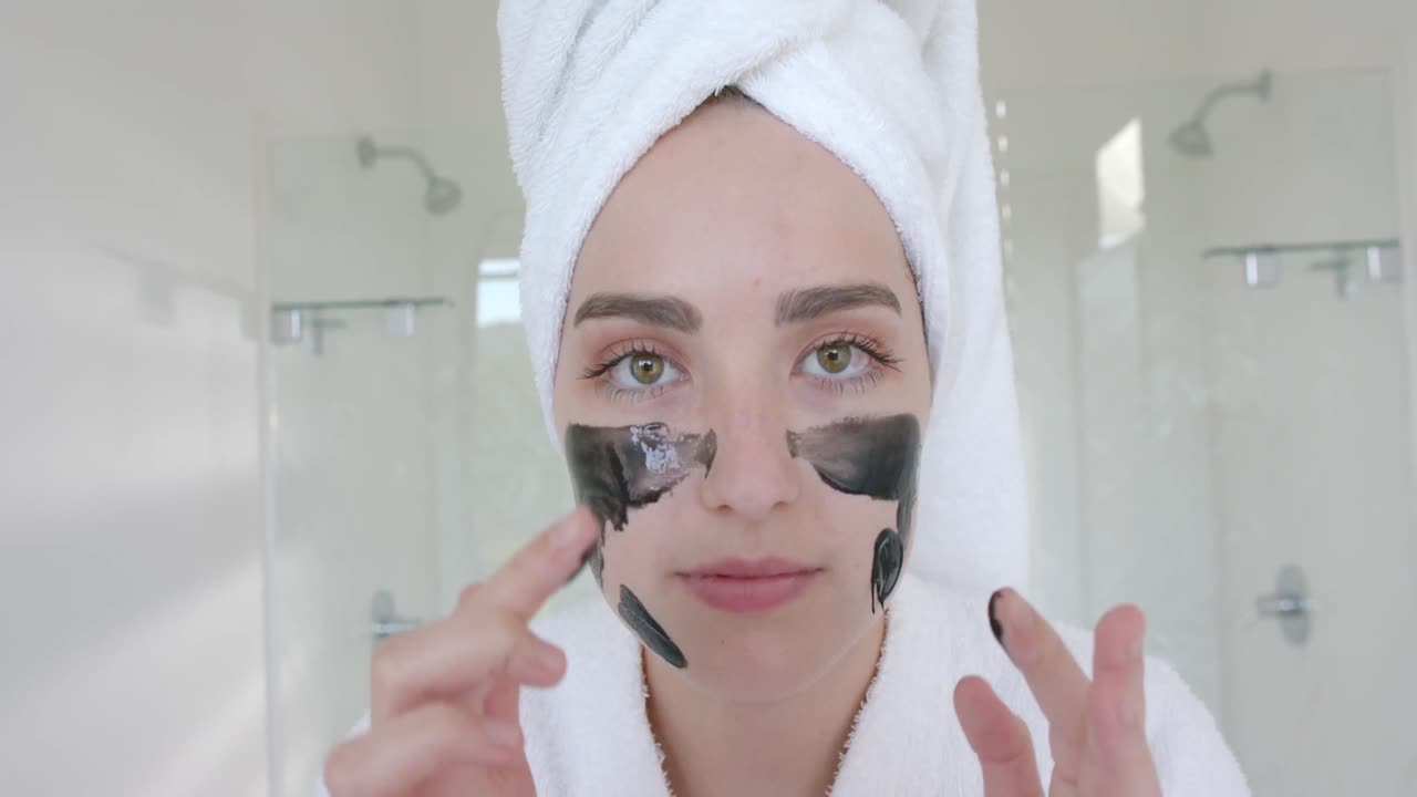 retrato de una mujer caucásica con una toalla en la cabeza haciendo una máscara facial en el baño en cámara lenta