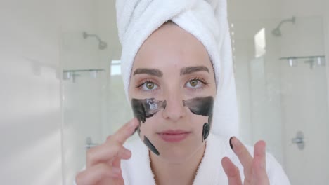 Portrait-of-caucasian-woman-with-towel-on-head-making-face-mask-in-bathroom-in-slow-motion