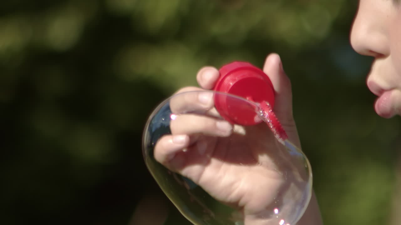 Child blows bubble that pops in slow motion, close-up
